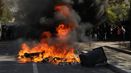 FILE PHOTO. Protesters burn trash bins during clashes with riot police near Paris on October 1, 2026