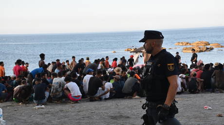 A police officer watches as migrants receive medical care from Red Cross volunteers  in Ceuta, Spain, August 7, 2026