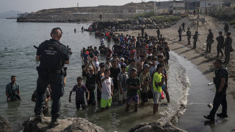 Members of the Guardia Civil USECIC guard migrants on Tarajal beach after crossing the border between Spain and Morocco on July 31, 2026 in Ceuta, Spain.