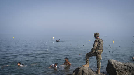 A member of the armed services watches over migrants crossing the border between Spain and Morocco on July 31, 2026 in Ceuta, Spain.