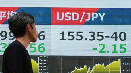 A person walks past an electronic board showing the US dollar and Japanese yen exchange rate in Tokyo, August 3, 2026