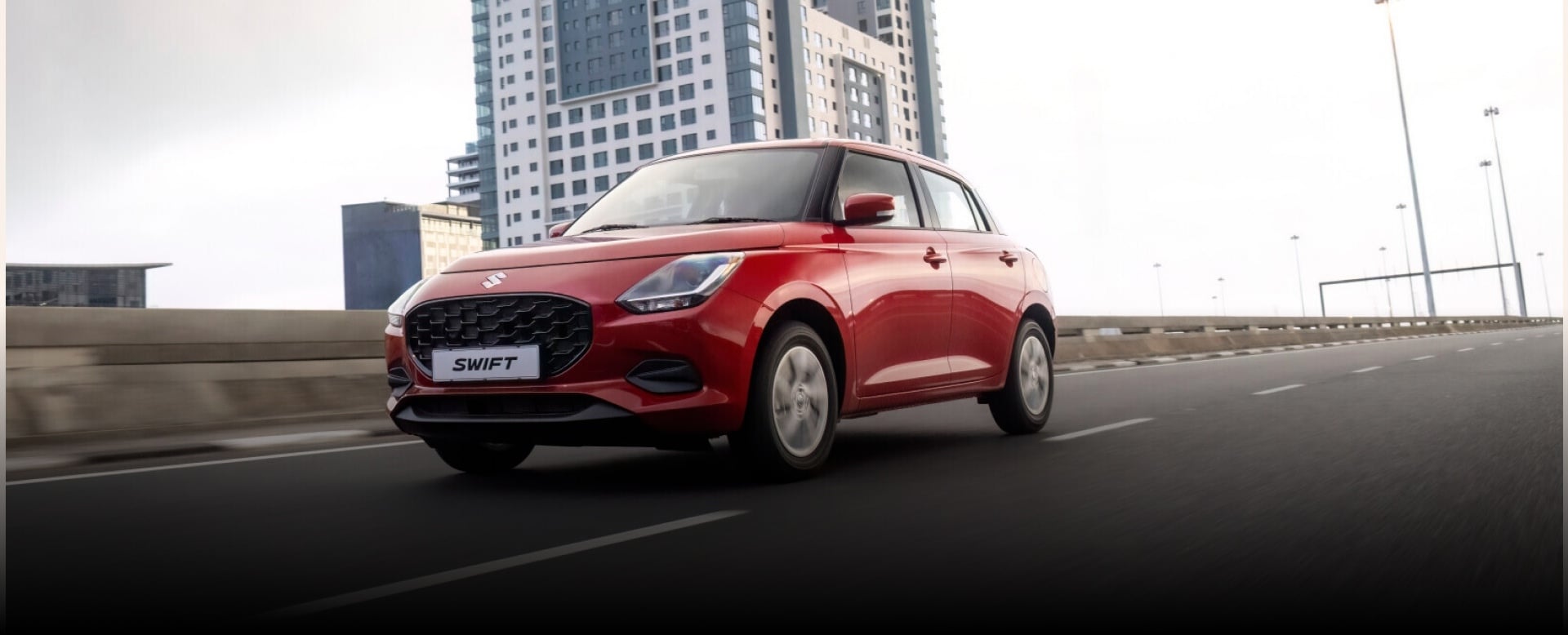 Red Suzuki Swift on the road with building behind 