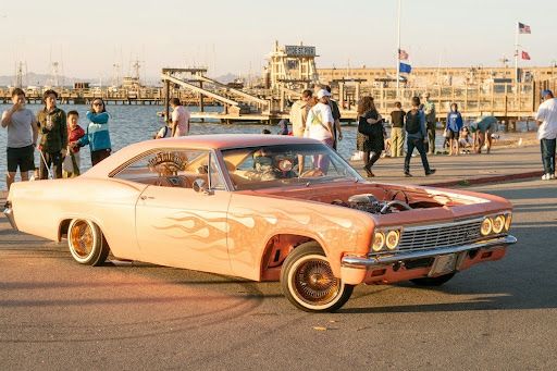 Custom classic car with flame paint and wire wheels parked near a waterfront