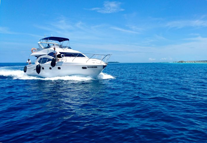 White recreational motorboat cruising across blue water beneath a clear sky